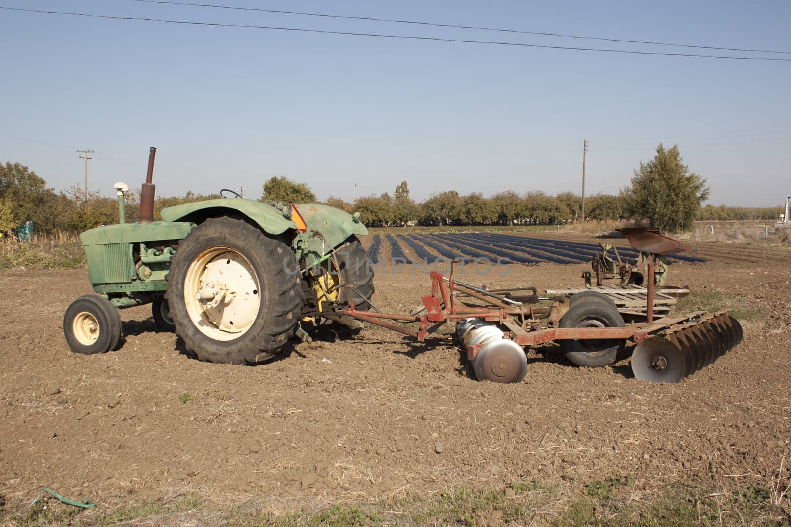 a farm tractor with a plow on the back with farm rows in the background.