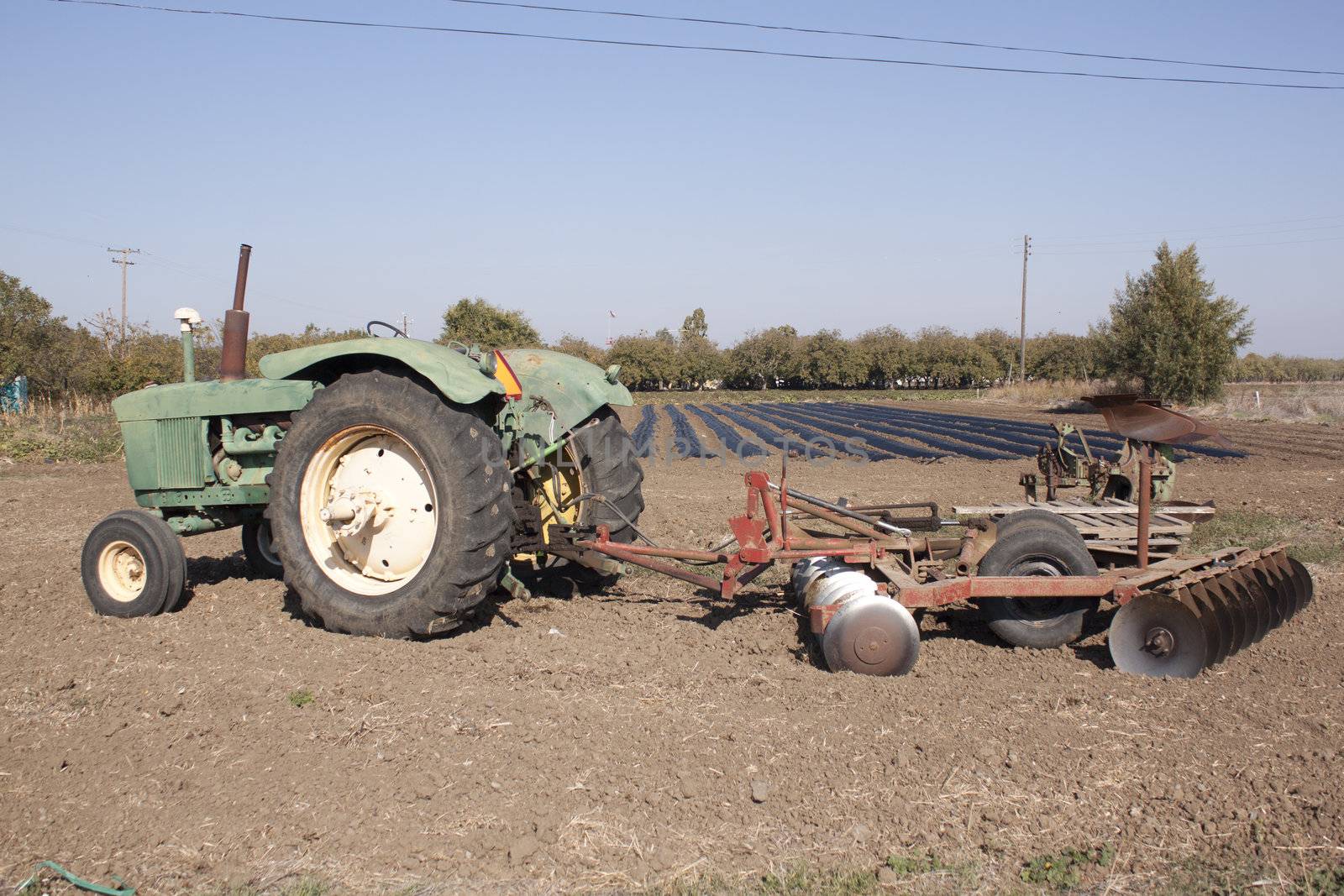 a farm tractor with a plow on the back with farm rows in the background.