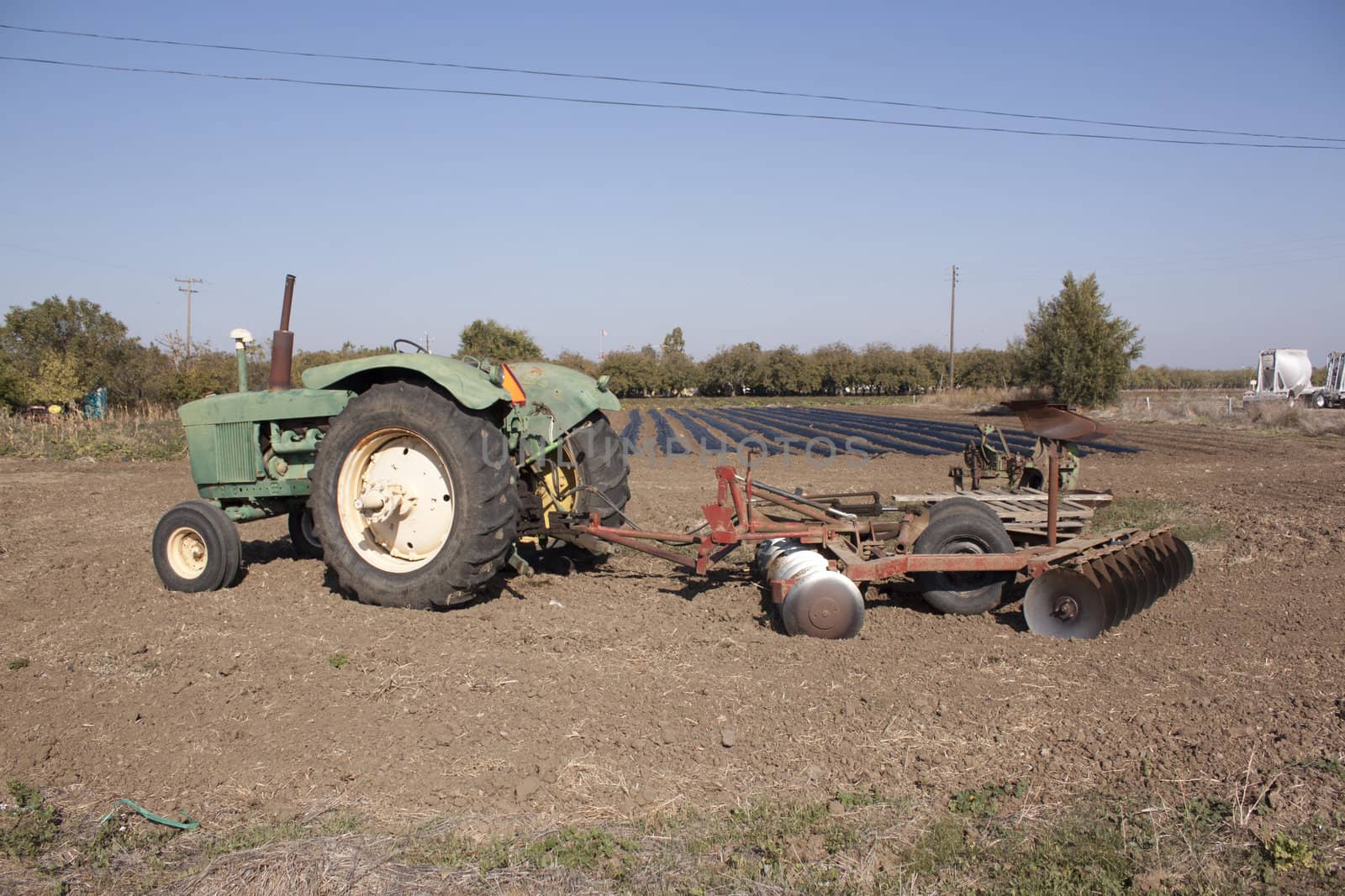 a farm tractor with a plow on the back with farm rows in the background.