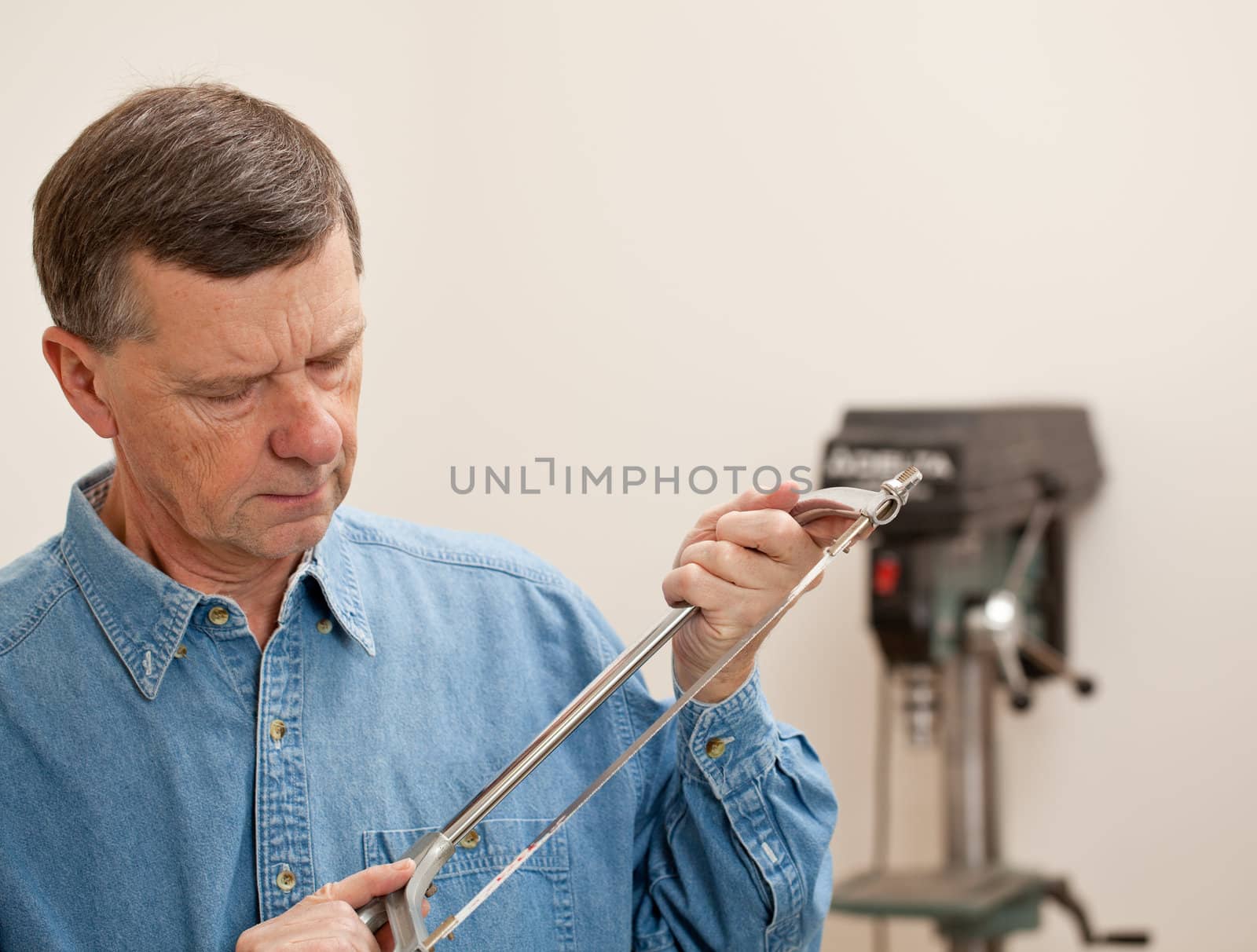 Senior male in a home workshop facing the camera and holding a metal saw