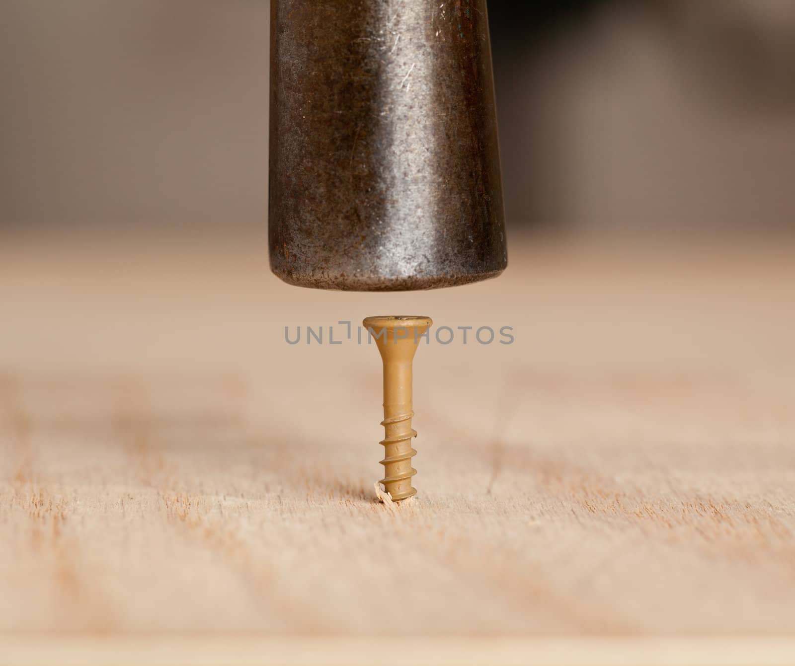 Brown screw being driven into wood by hammer head