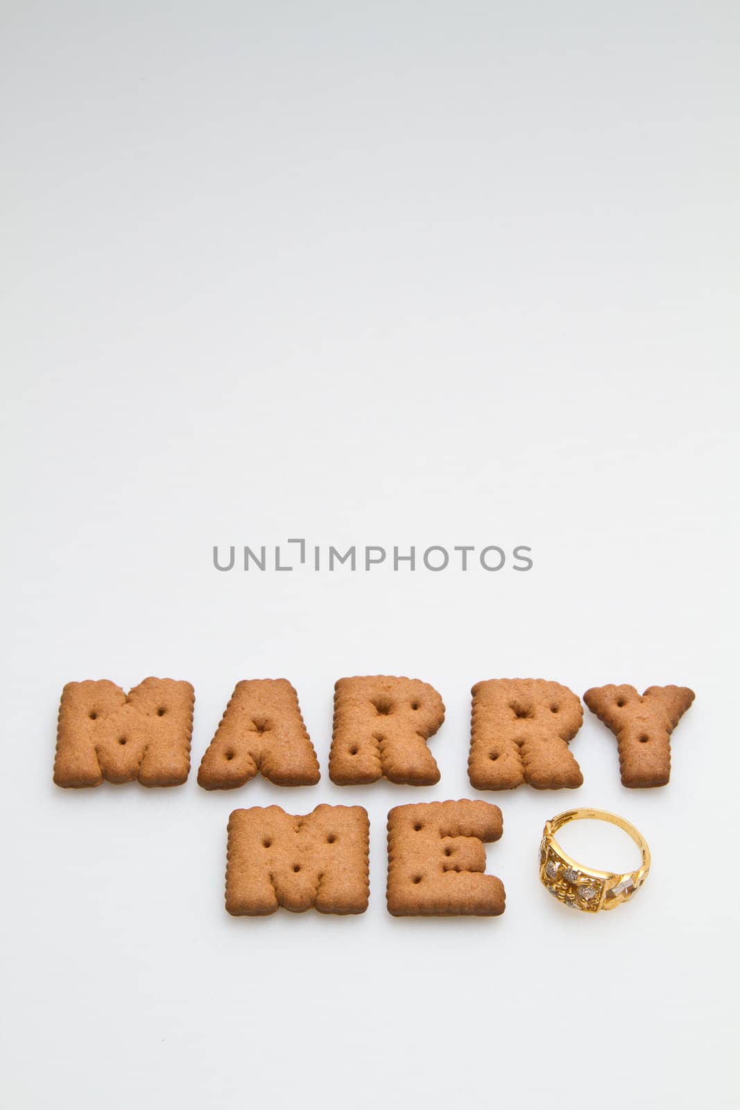 Marry me wording from brown biscuits with gold ring on white surface portrait orientation