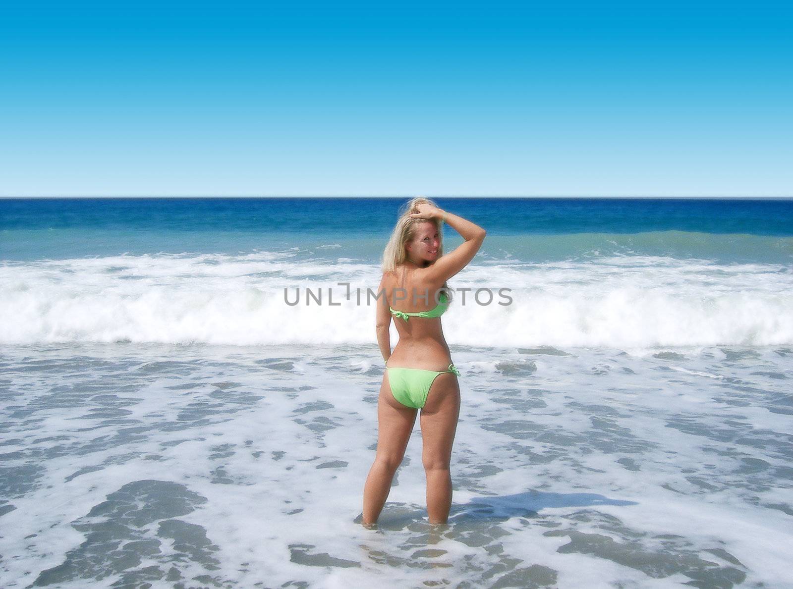 blond woman posing on the beach, standing with raised hand 
