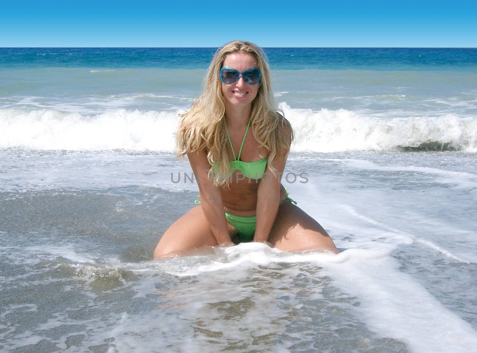 blond woman kneeling  in the surf on a beach 
