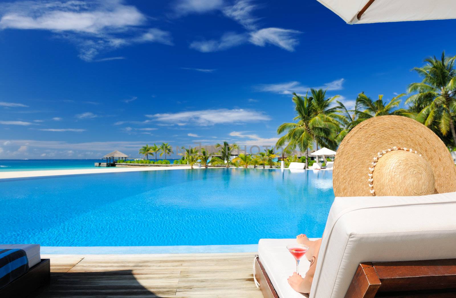 Woman in hat relaxing at the poolside with cosmopolitan cocktail