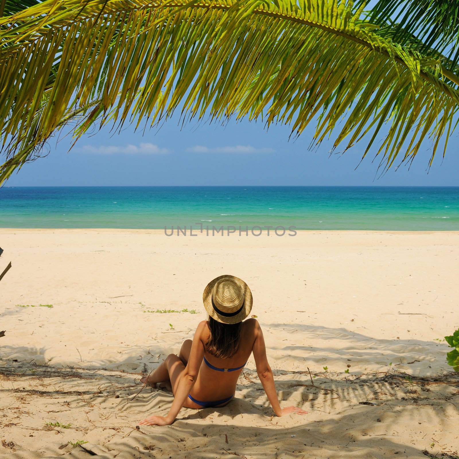 Woman at beach under palm tree with leaf shadow on her body