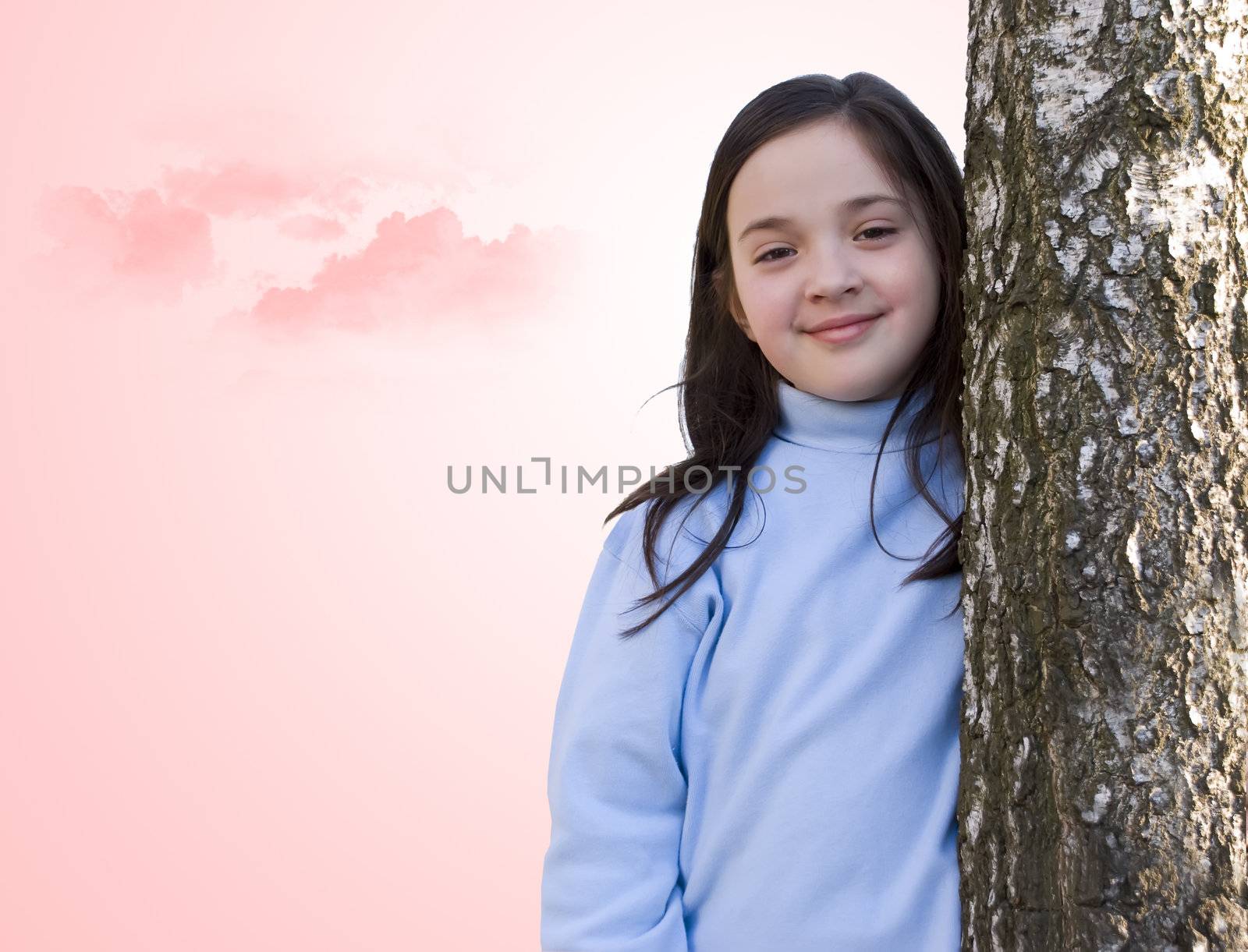 Beautiful little girl behind the tree, in the front of a pink sky