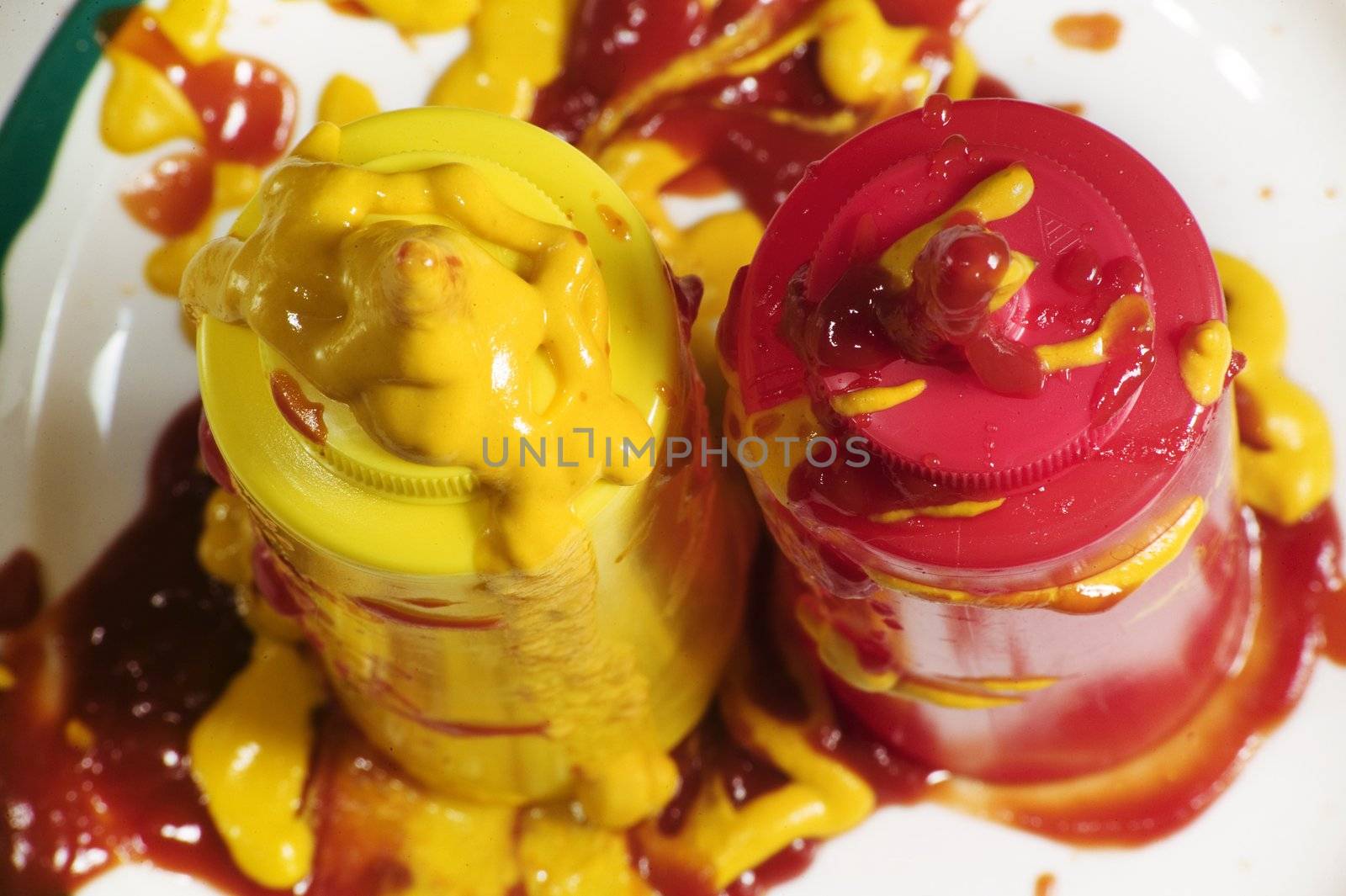Messy mustard and ketchup squeeze bottles standing up on a plate.