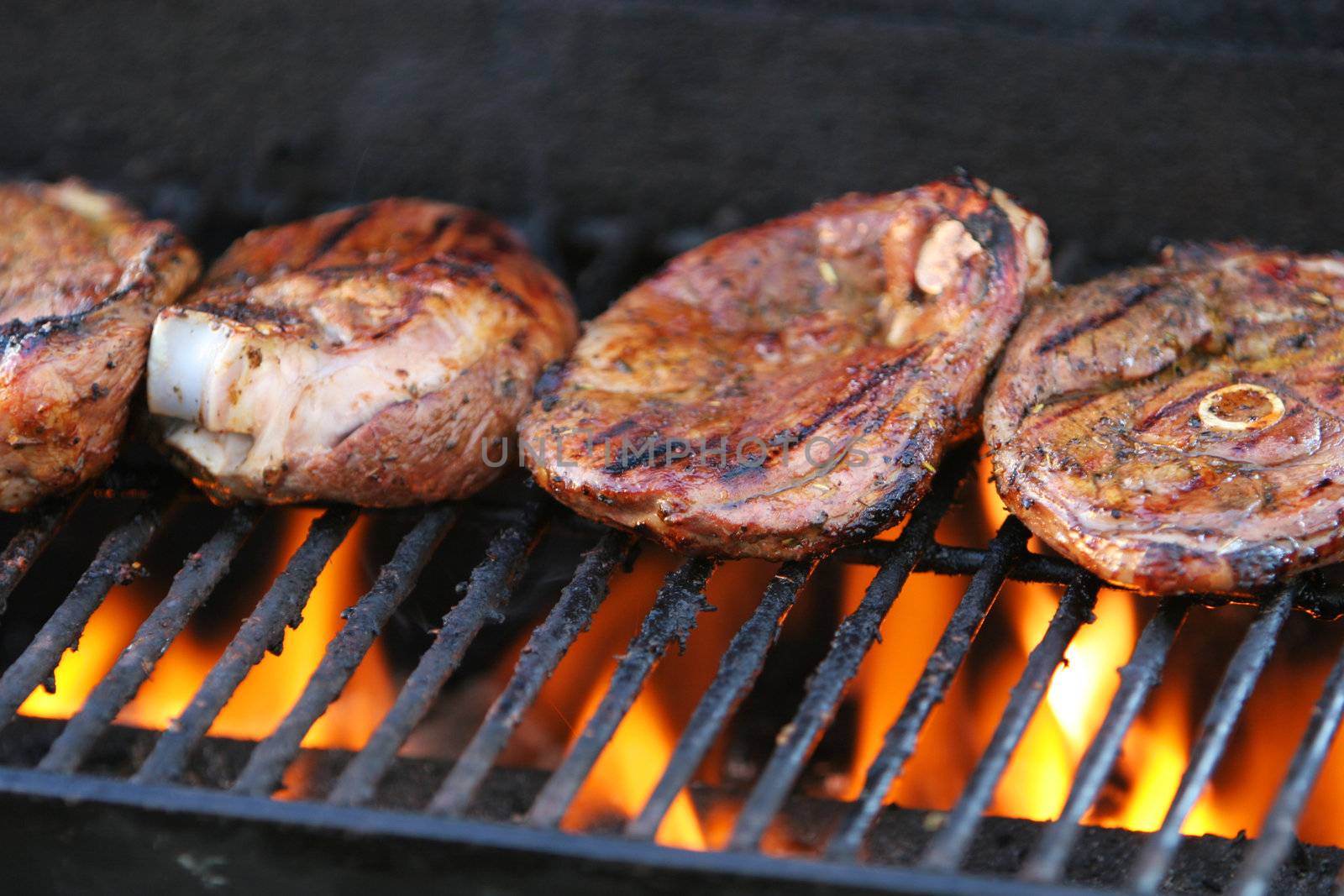 Lamb chops being barbecued on a gasgrill, flames visible beneath meat