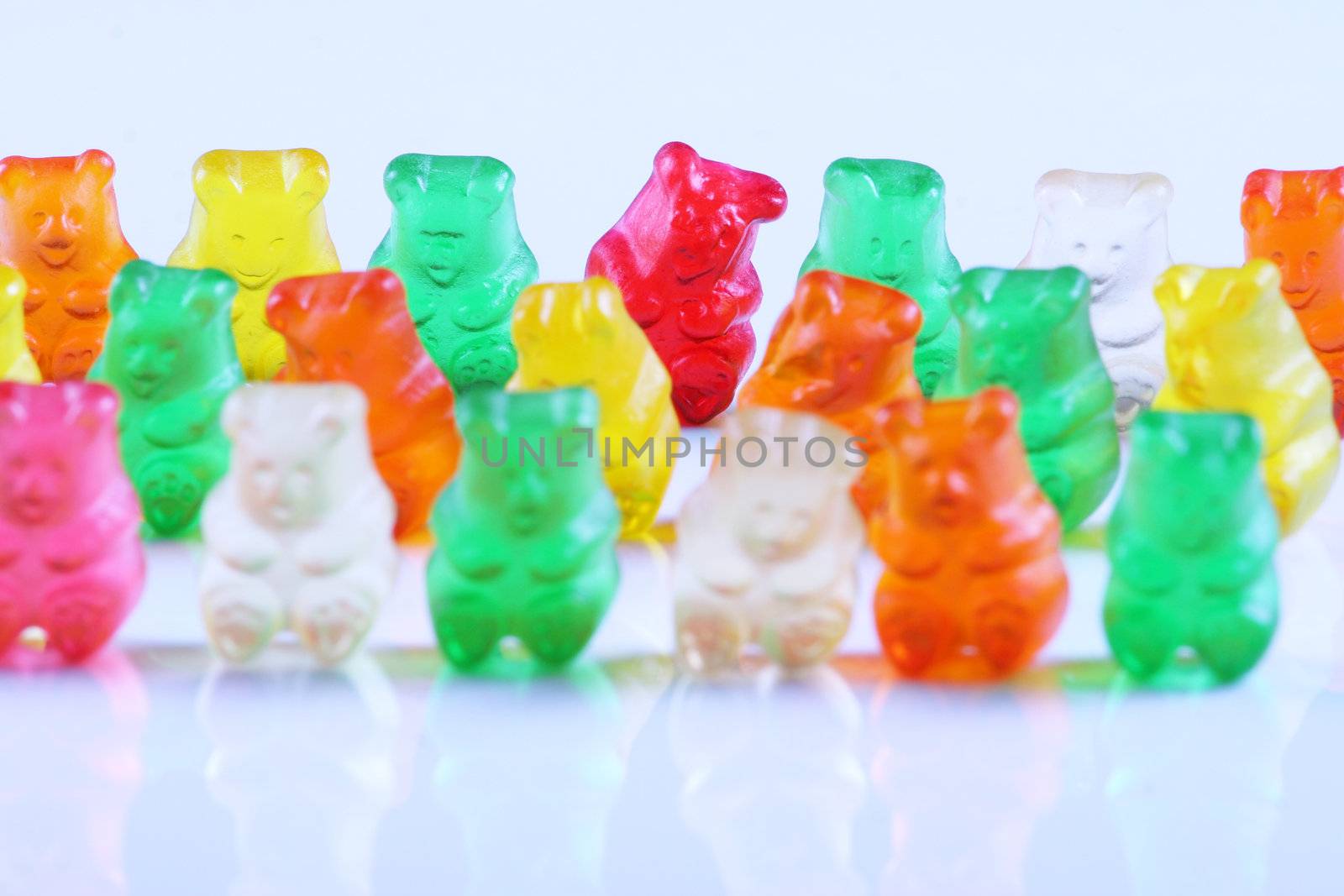 Colorful gummy bears lined up in rows, with the sole red bear being main focus. Isolated on white.;