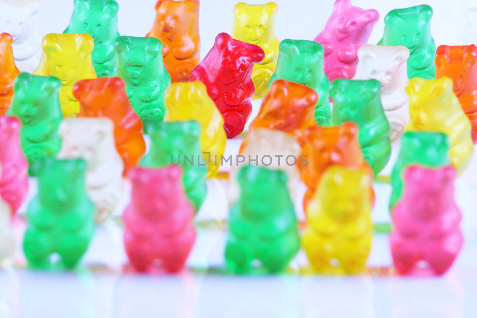 Colorful gummy bears lined up in rows, with the sole red bear being main focus. Isolated on white.;