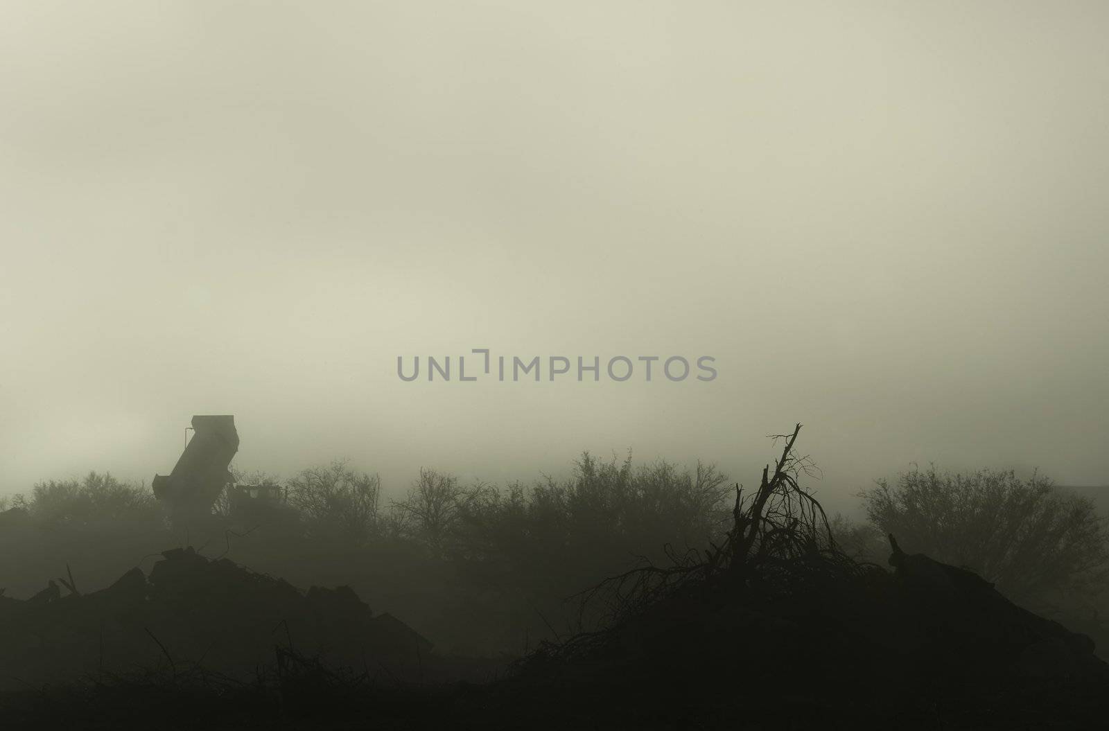 A dump turck on the horizon and debris in the foreground on a foggy day.