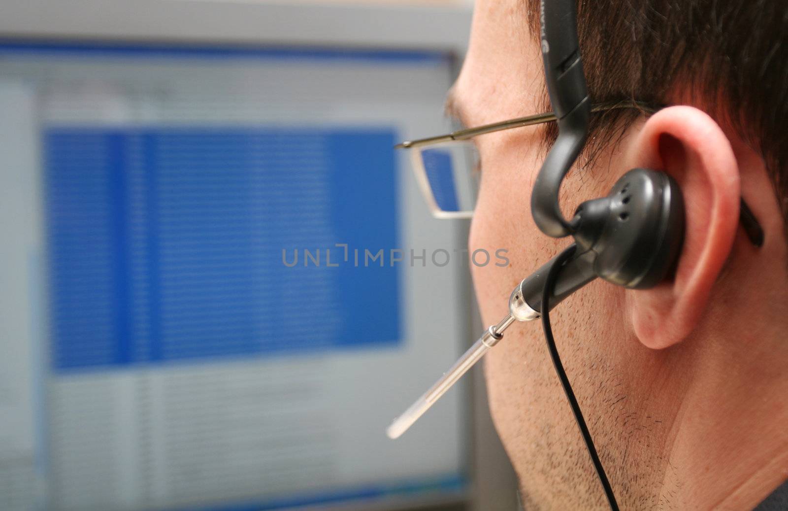 A male analyst working at a computer, with a headset, shot from behind focus on headset