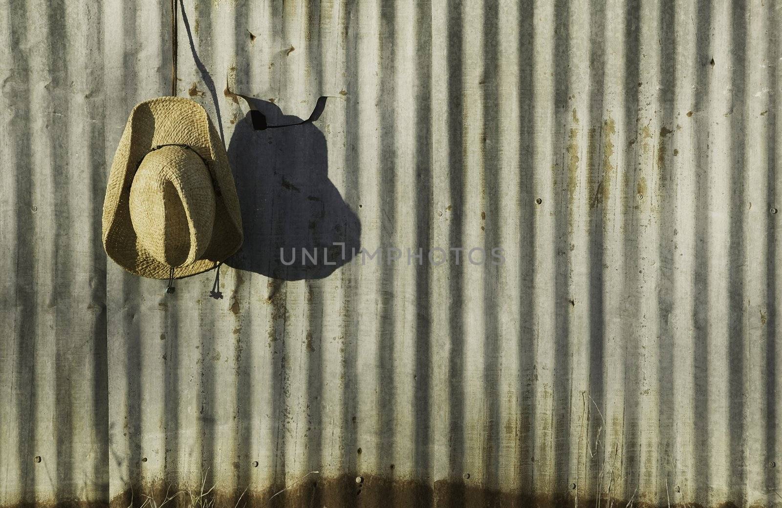 Straw cowboy hat hanging in front of old corrugated metal.