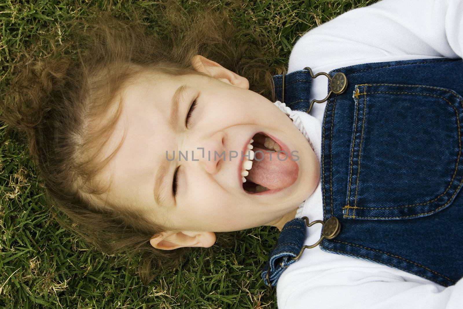 Little girl laying in the grass sticks out her tongue.