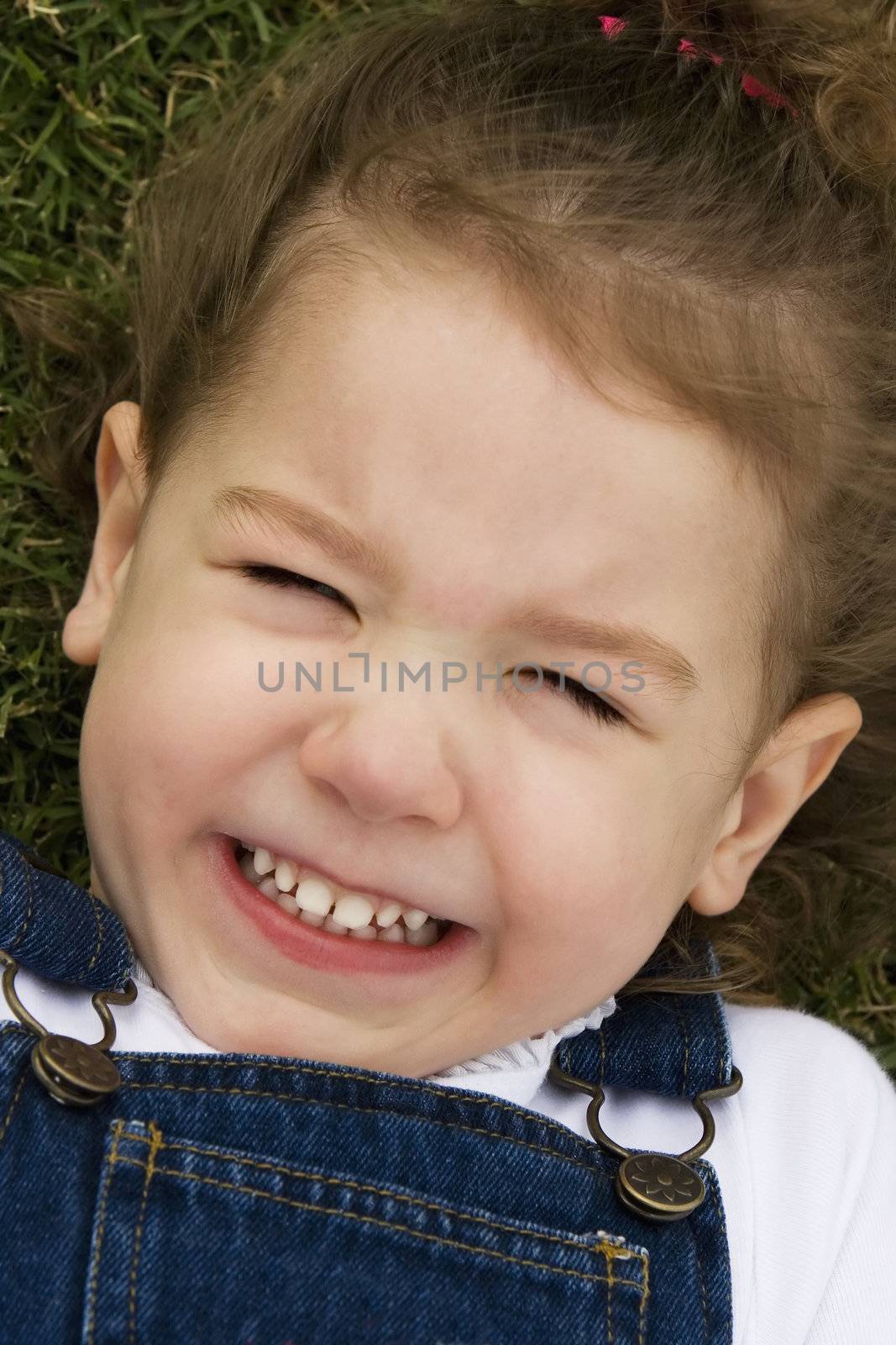 Little girl laying in the grass making a silly face with a big smile.