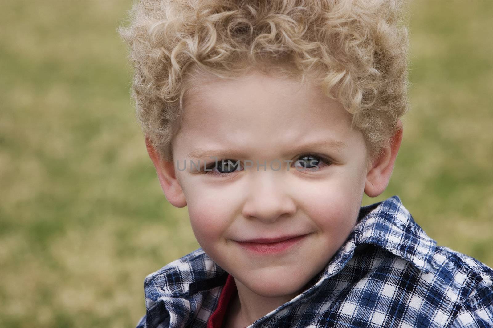 Smiling young boy in a plaid shirt with grass in the background