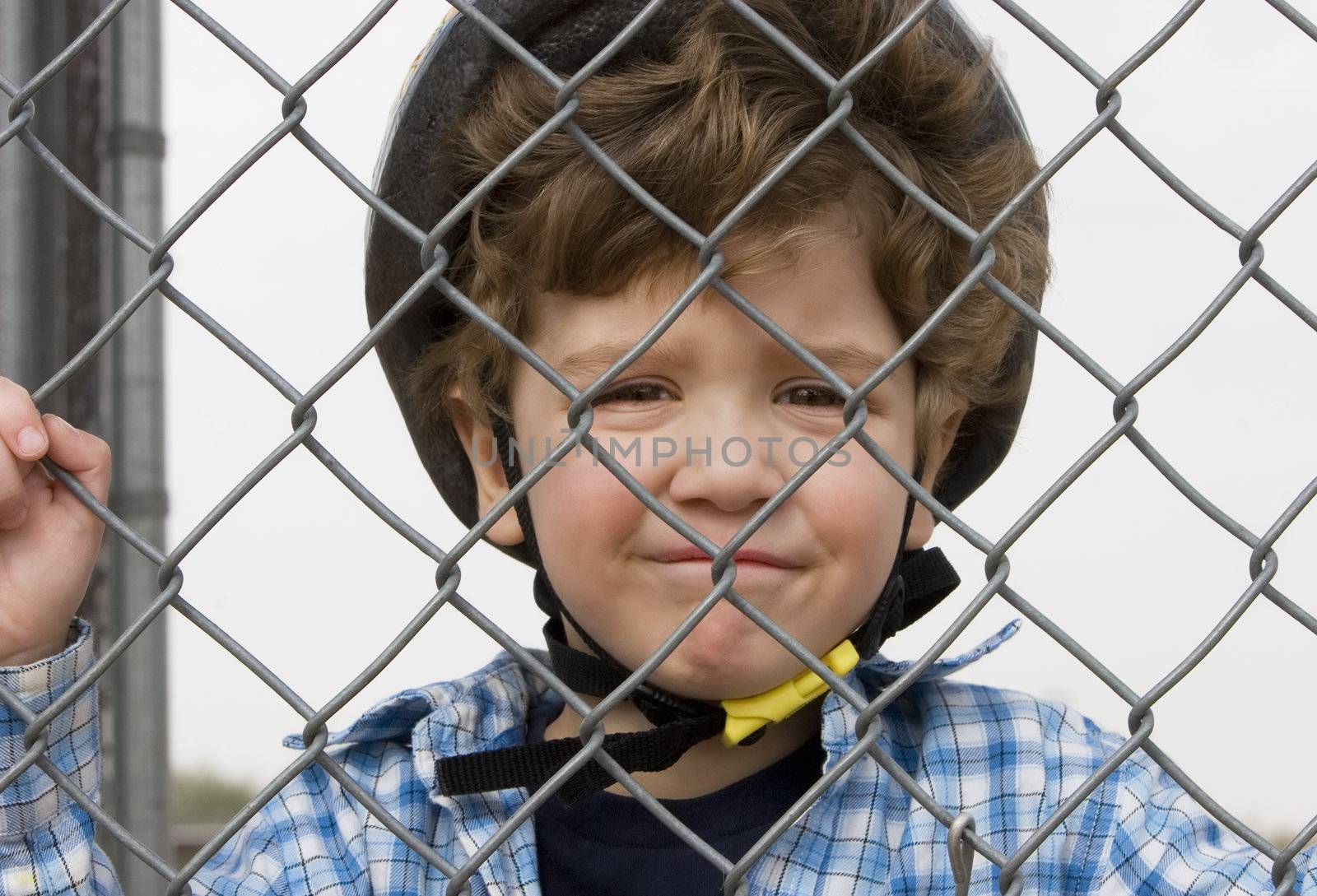 A little boy in a bicycle helmet behind chain link