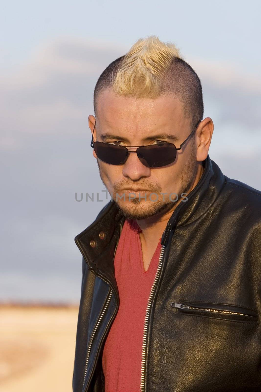 Man with a leather jacket and punk haircut stares at the camera.