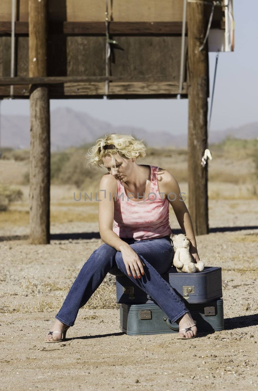 Unhappy blonde woman sitting on suitcases in a remote location