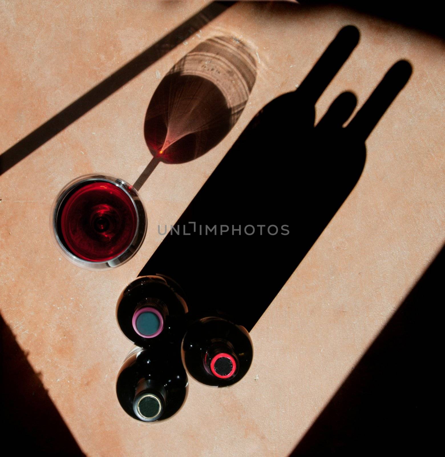Wine bottels and wine glass with heavy side-light and long, dramatic shadow. 