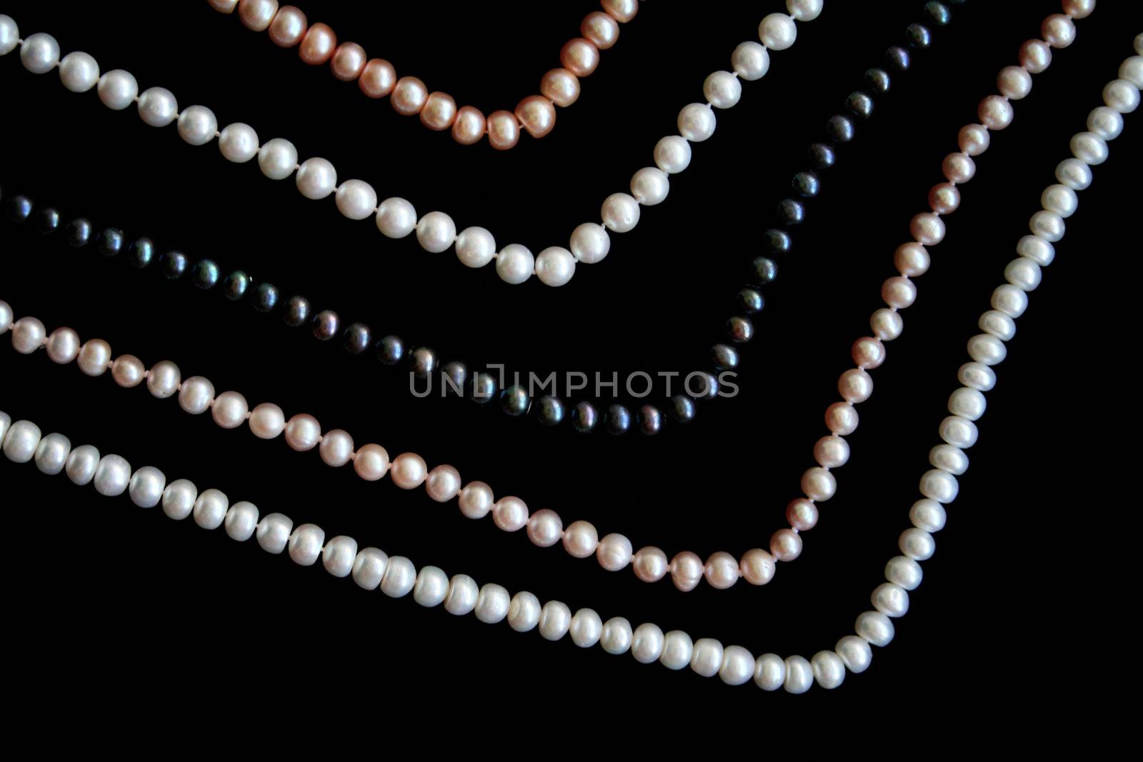 White, black and pink pearls on the black silk as background 