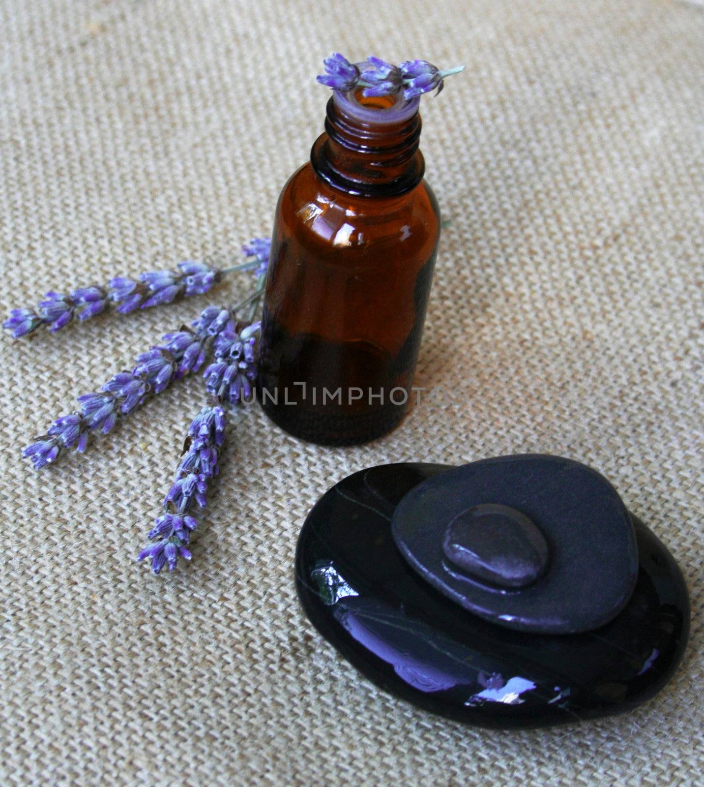 Lavender flowers, bottle of essential oil and black stones on sackcloth background in a spa composition