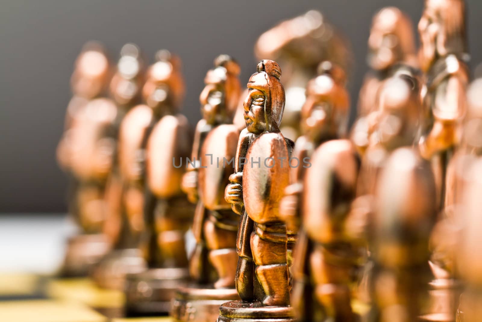 Brass chess piece in focus with other blurred pieces image and grey background
