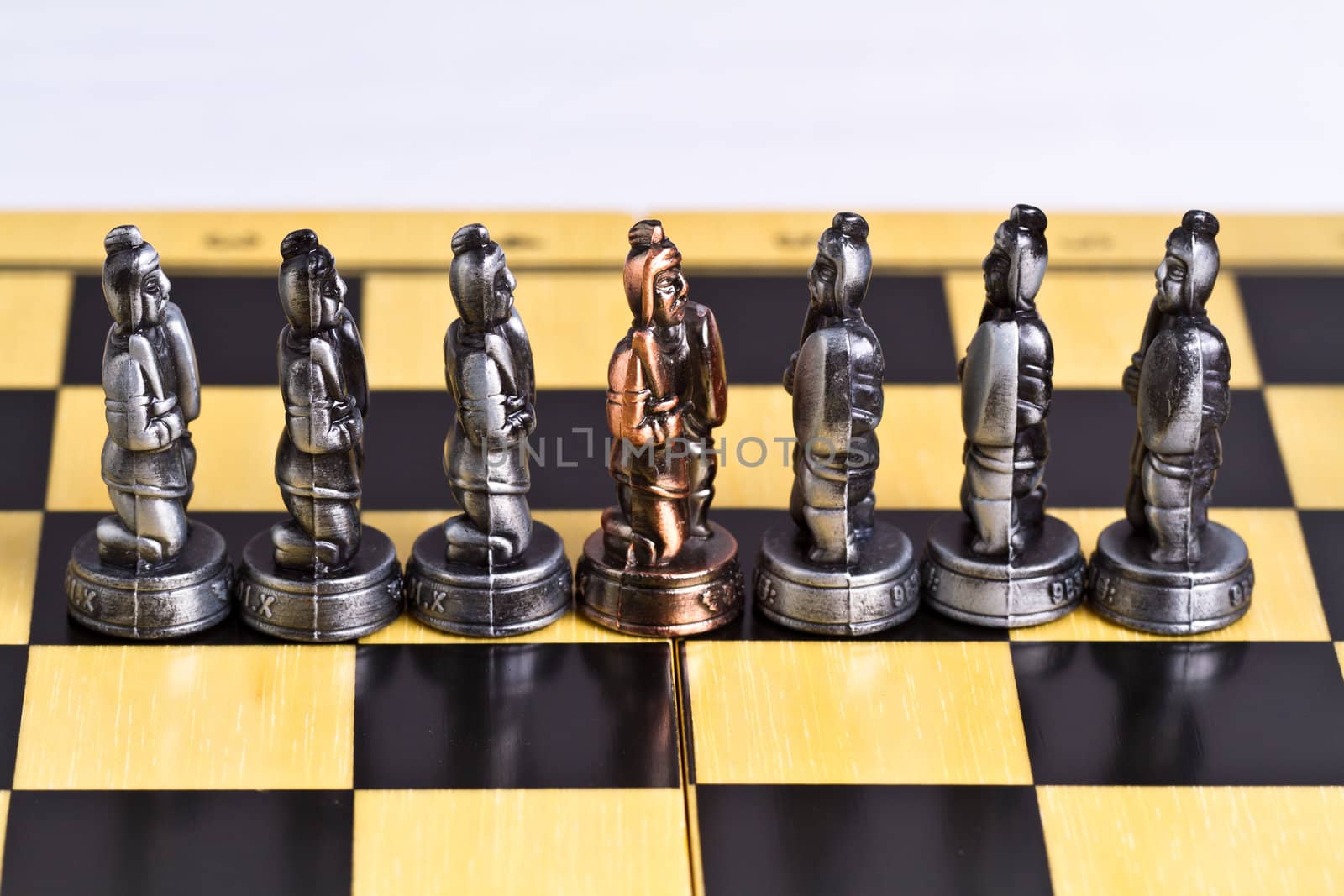 a brass pawn piece among the silver pieces on a checker board