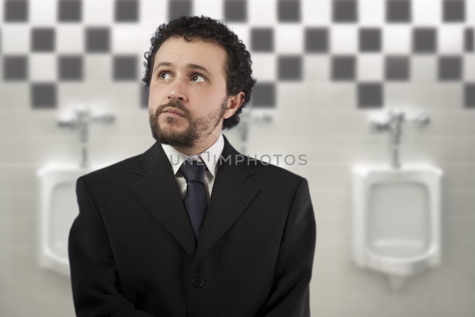 businessman with a distracted look urinating in urinals