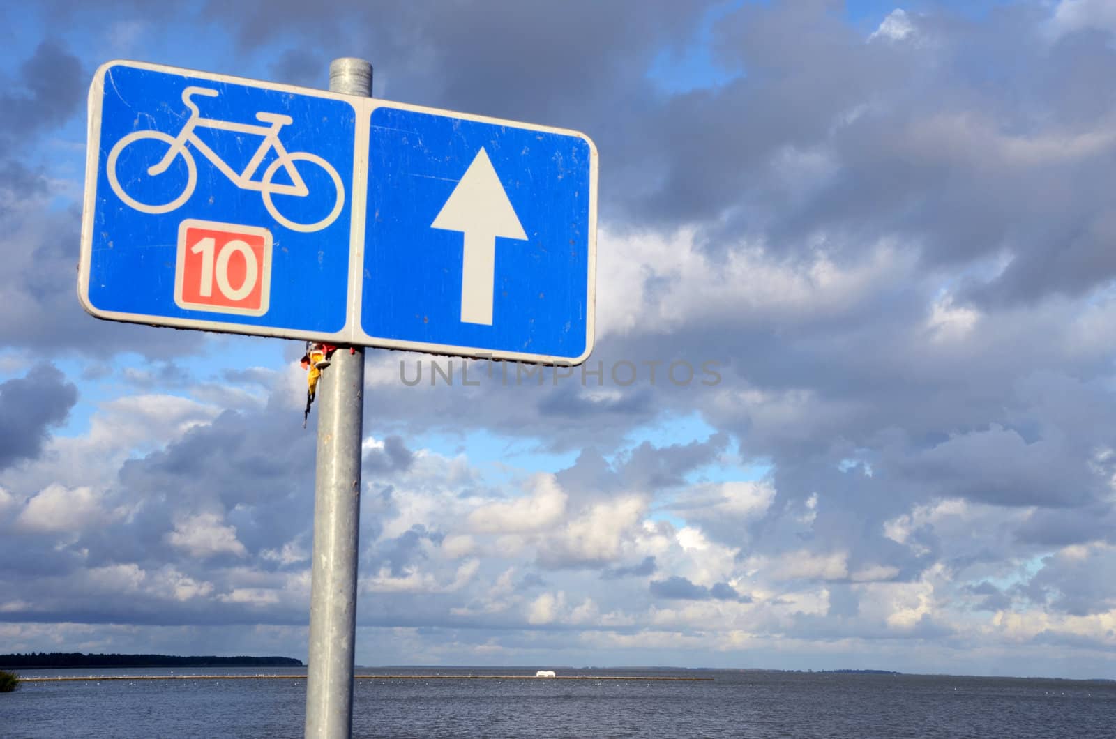Bicycle path sign number ten 10 near lake and cloudy blue sky.