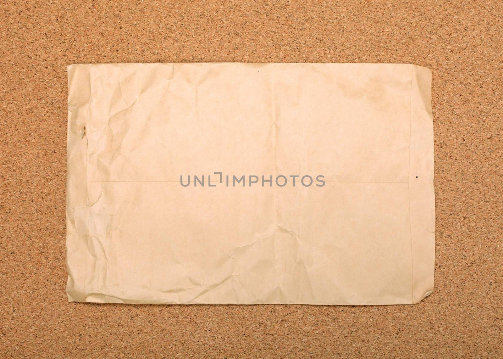 Wrinkled brown envelope attached to cork board. As backdrop or background.