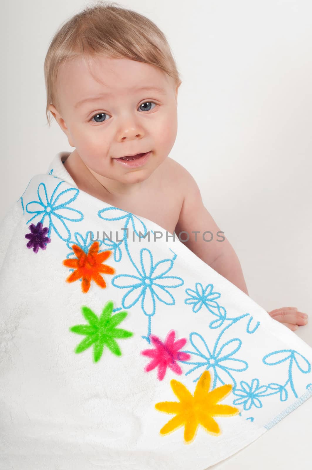 Happy little boy in white blanket with flowers in studio