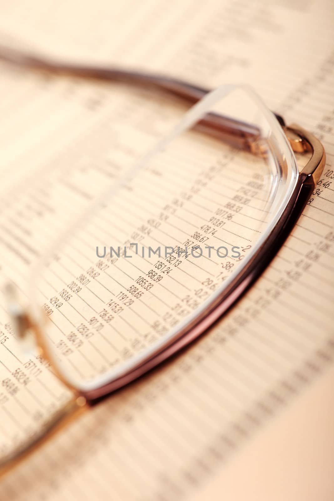 Macro of financial data through eyeglasses, laying on newspaper.