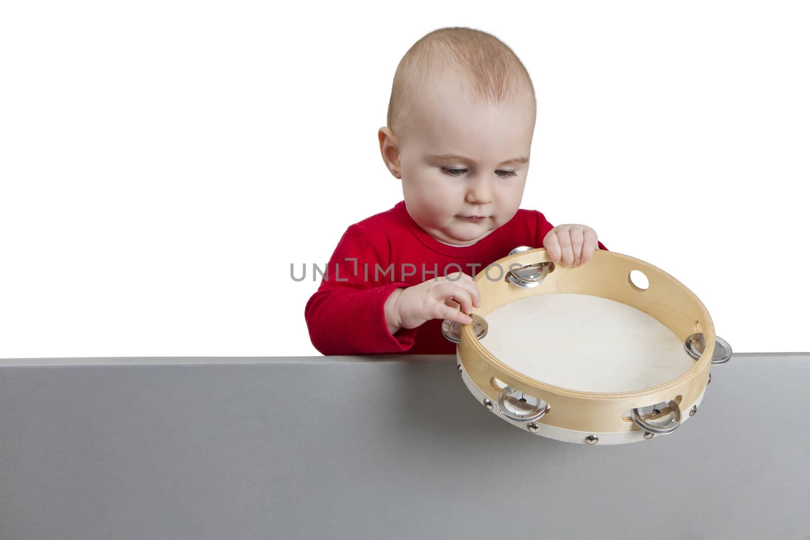 young child holding tambourine behind grey shield. isolate on white background