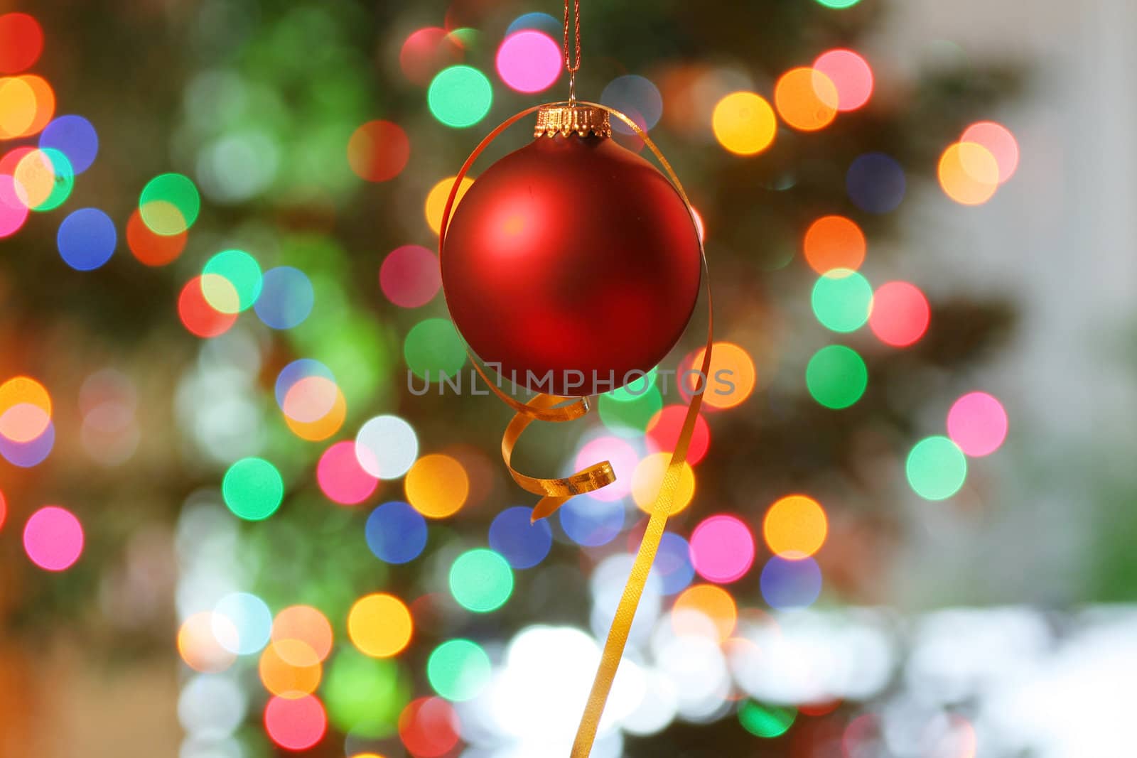 Red frosted Christmas ornament with colorful lights in background.