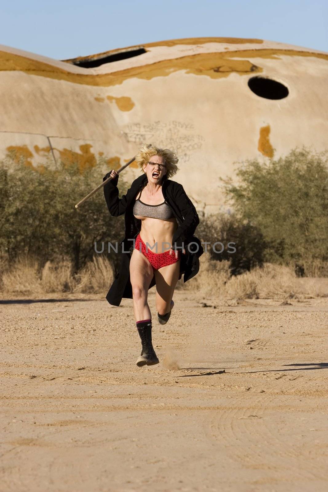 Female science fiction model in a desolate location attacking with a wooden stick.