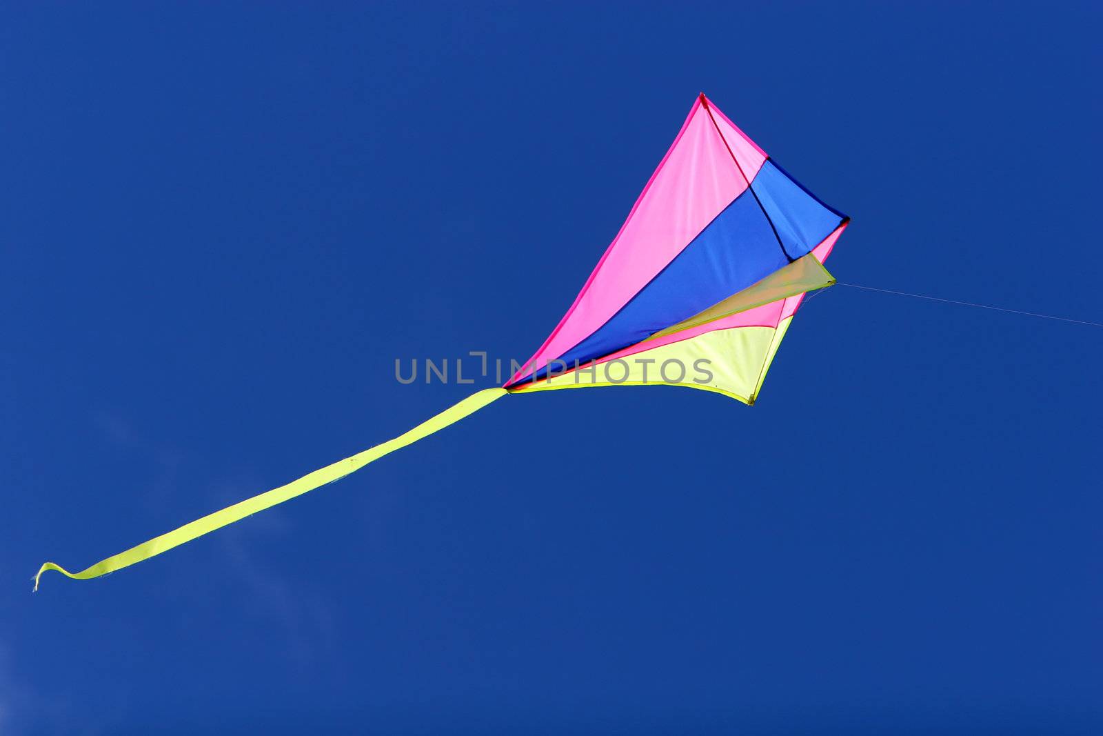 a kite flying against a blue sky in sunlight, bright colors and streaming tail