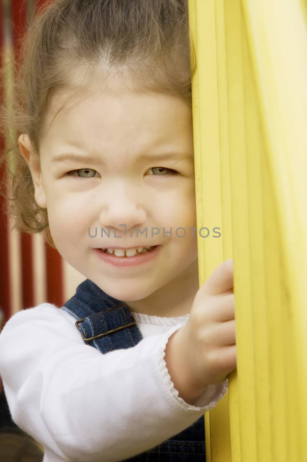 Little girl on play equipment smiles at the camera
