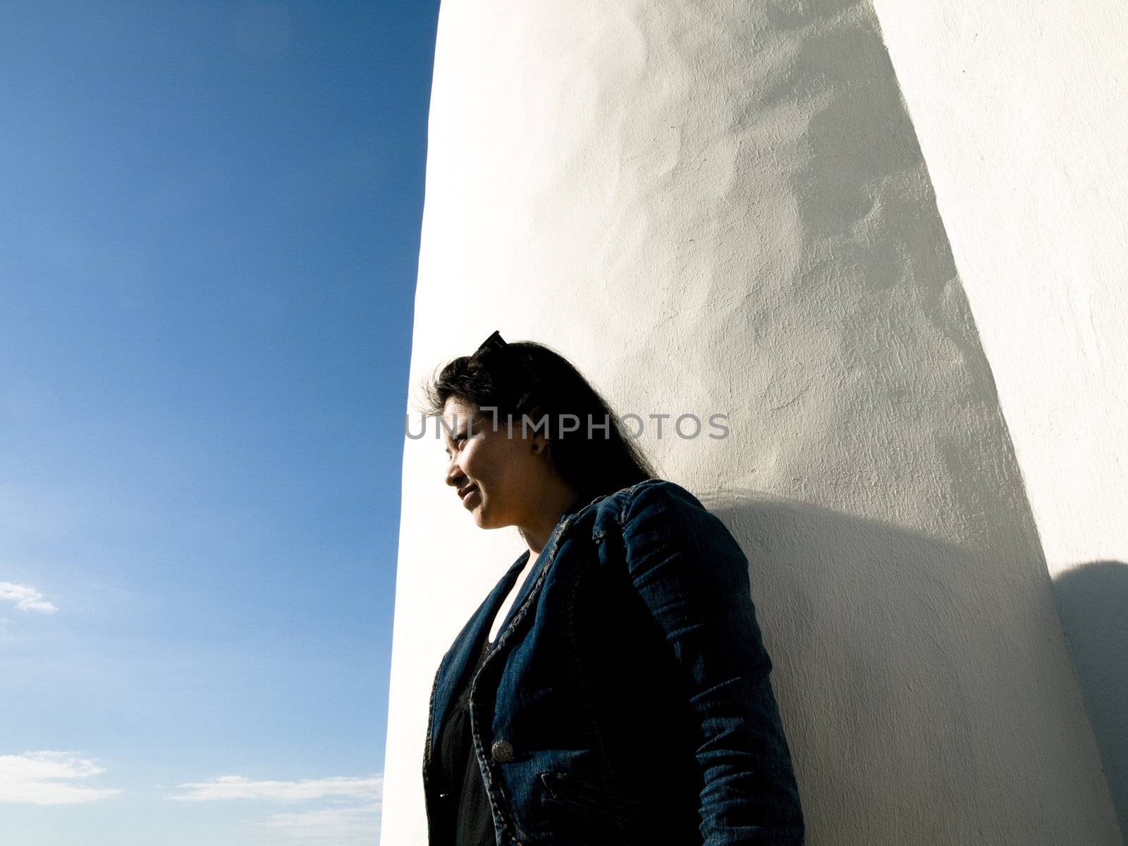 Thai girl standing by a white wall looking at the seashore