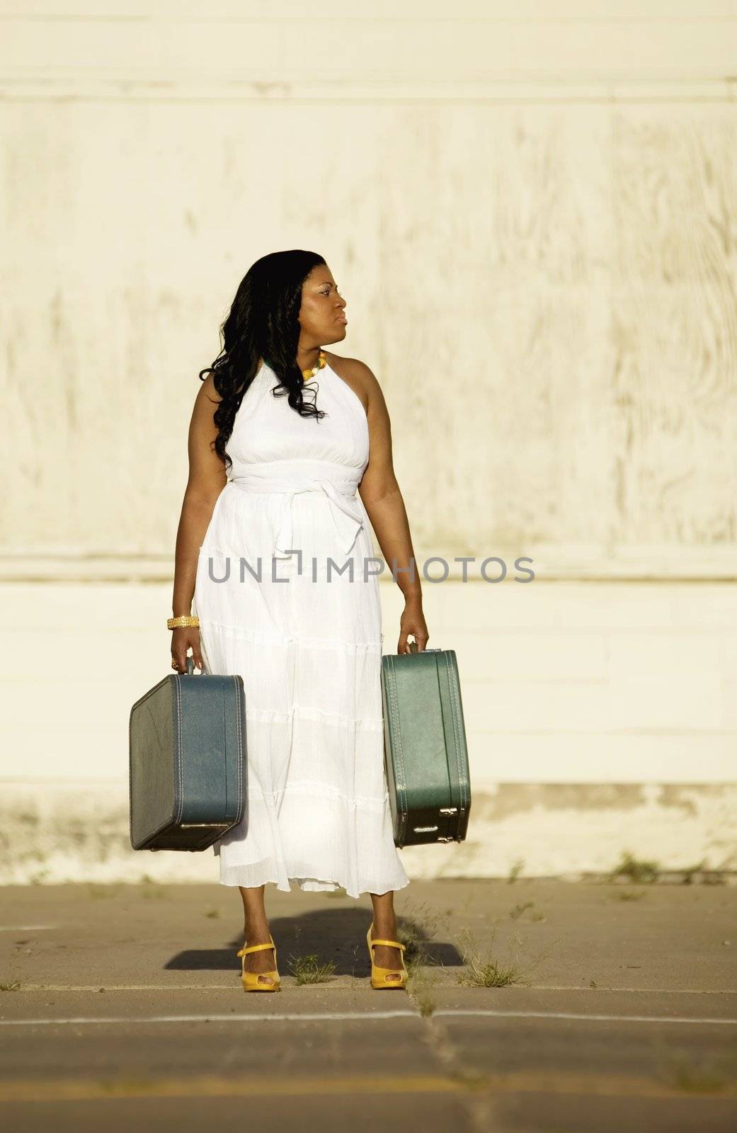 African American woman with suitcases waiting by the street for someone to arrive.