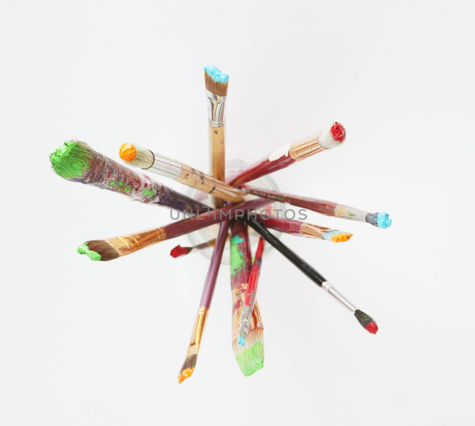 Paintbrushes in a glass jar against a white background, shot from above.