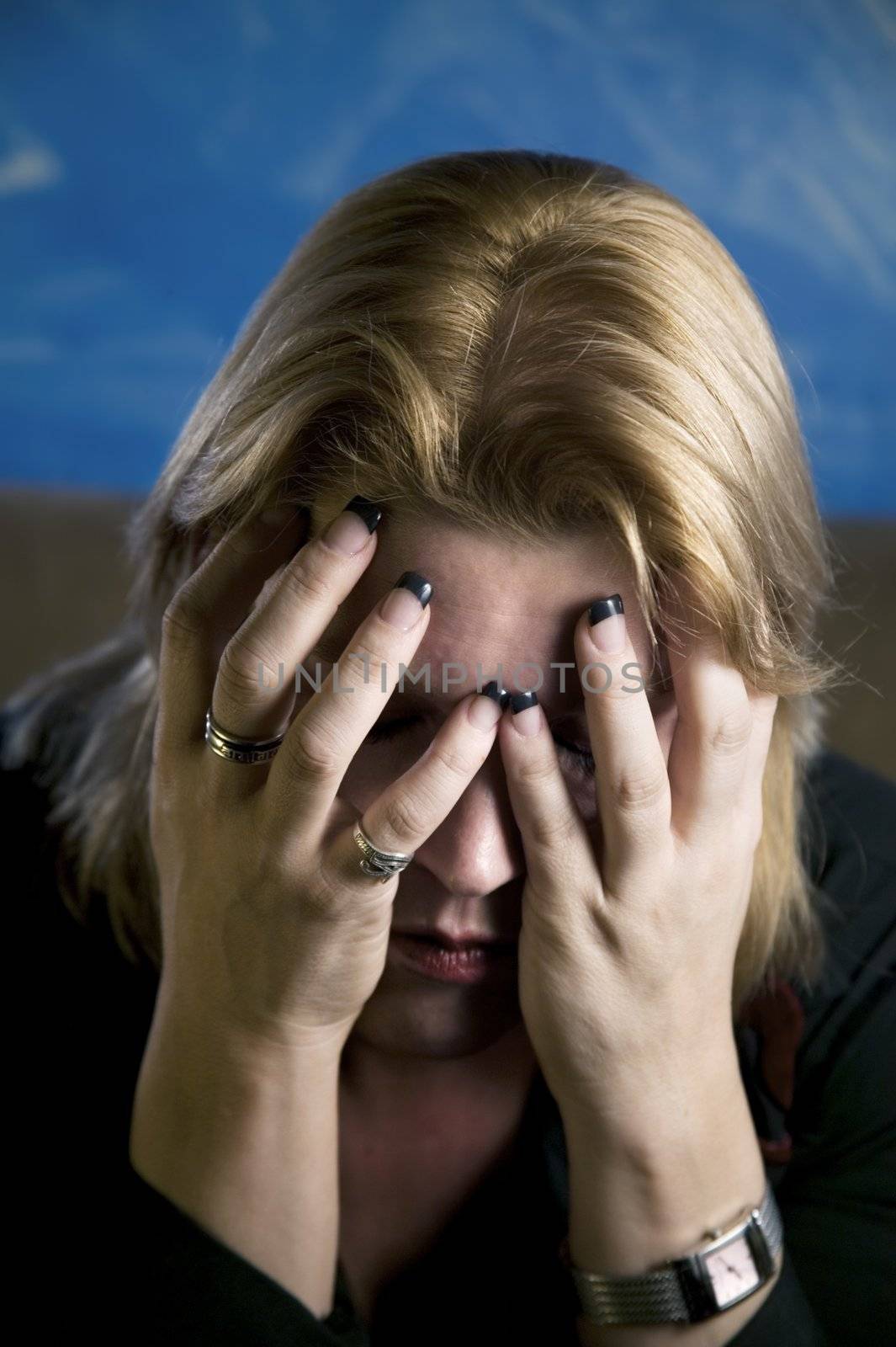 Close up of blonde woman in a studio setting hiding her face in her hands.