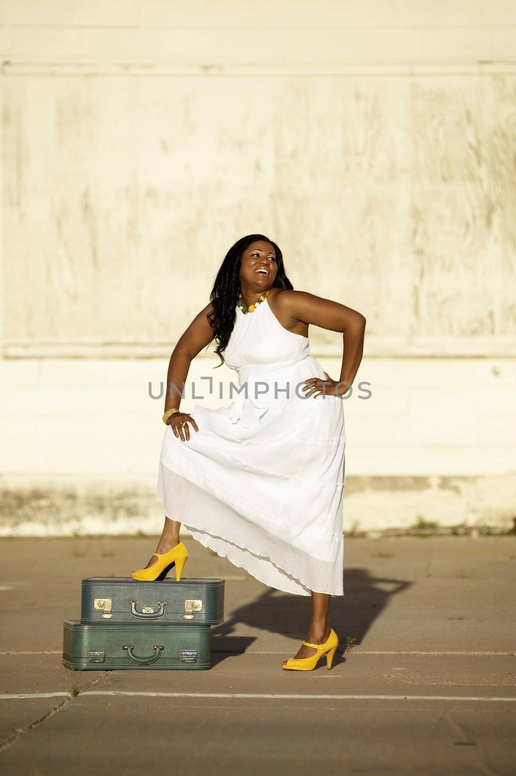 African American woman with suitcases waits and laughs outside an industrial building.