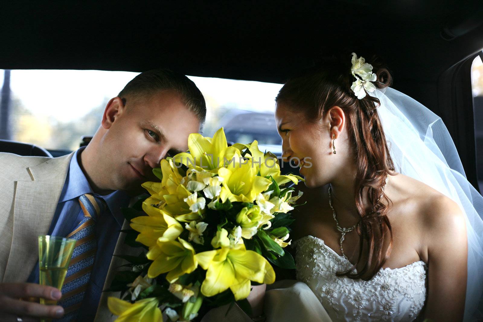The groom and the bride with a bouquet from lilies in the automobile