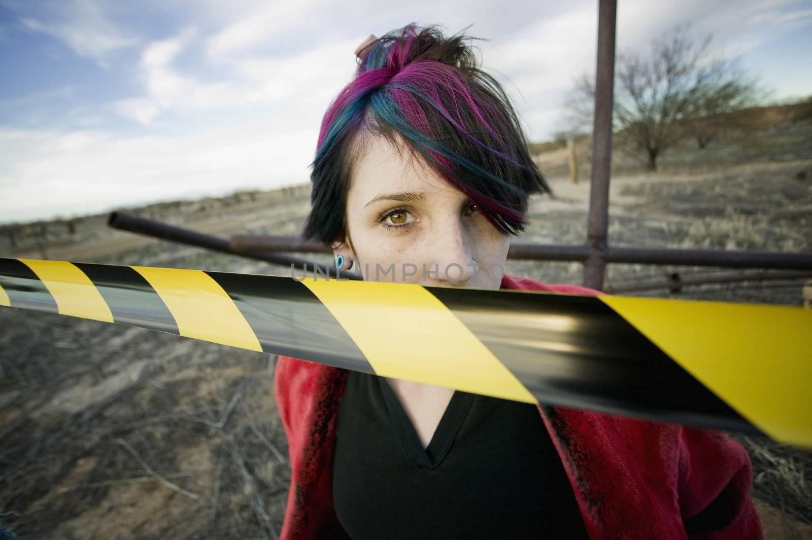 Punk girl outdoors behind a strip of yellow and black caution tape