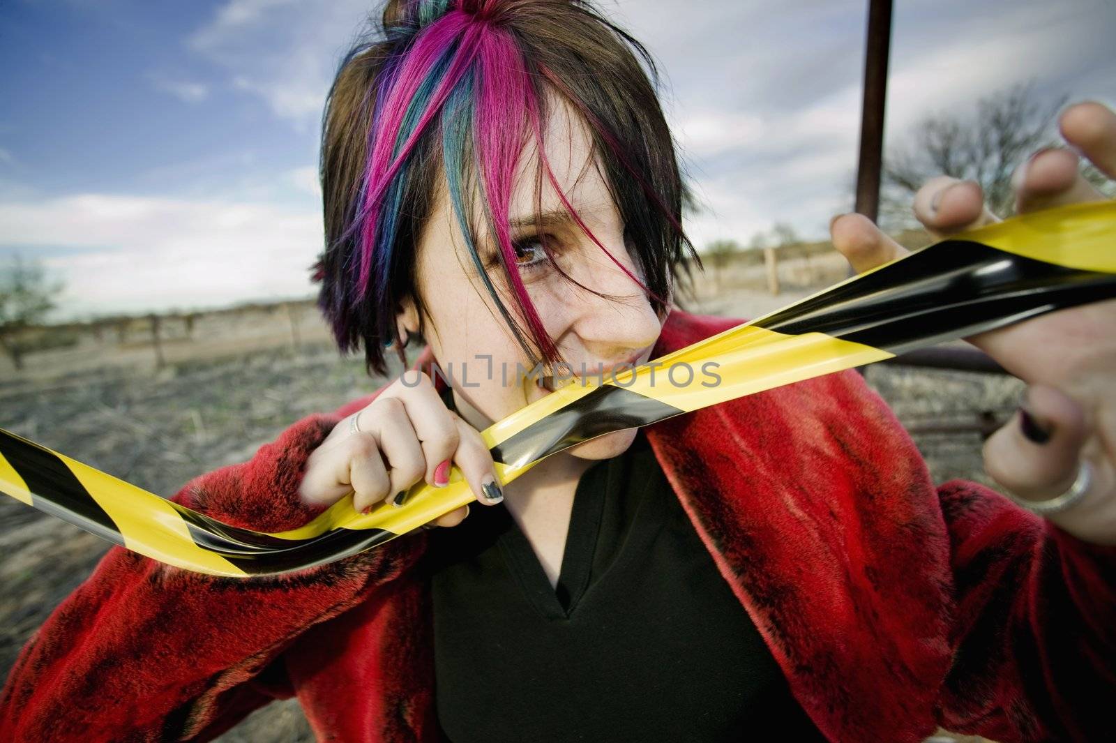 Punk girl outdoors biting a strip of yellow and black caution tape