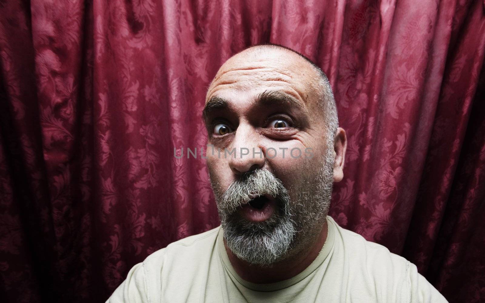 Man making a funny face in front of red curtains by Creatista