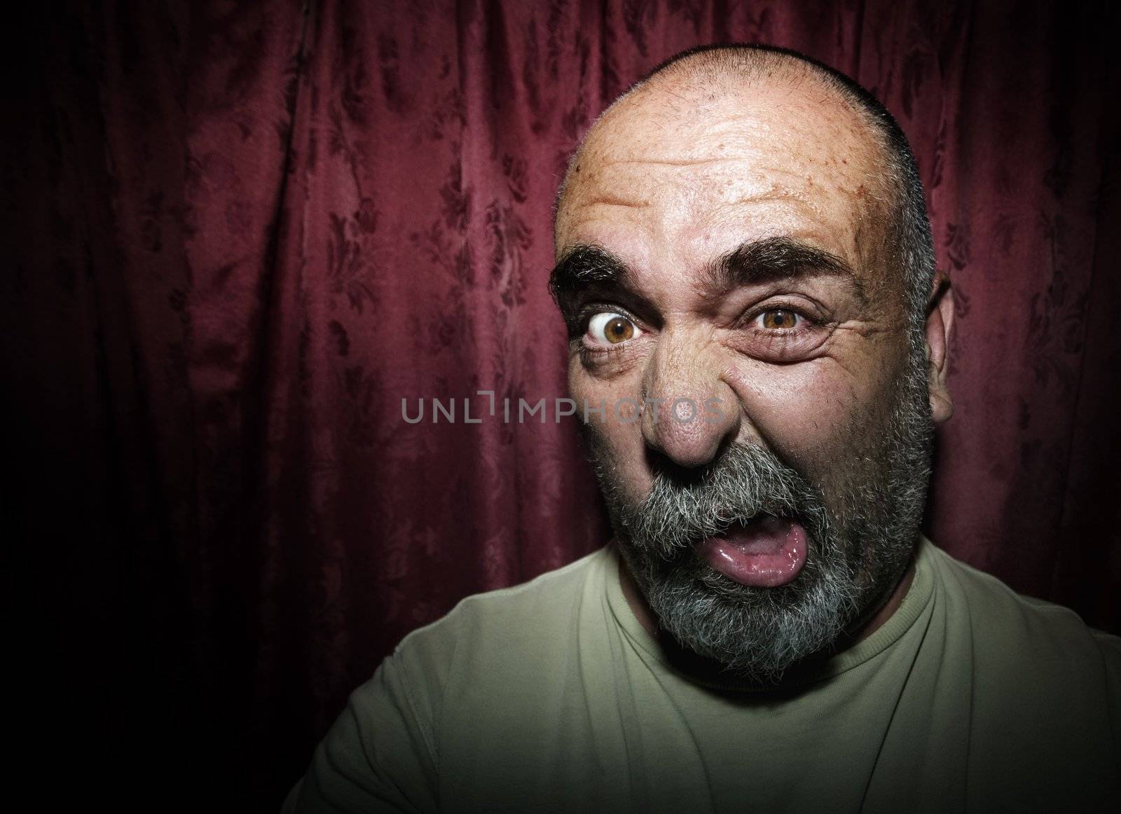 Close-up of a man in front of red curtains making a funny face