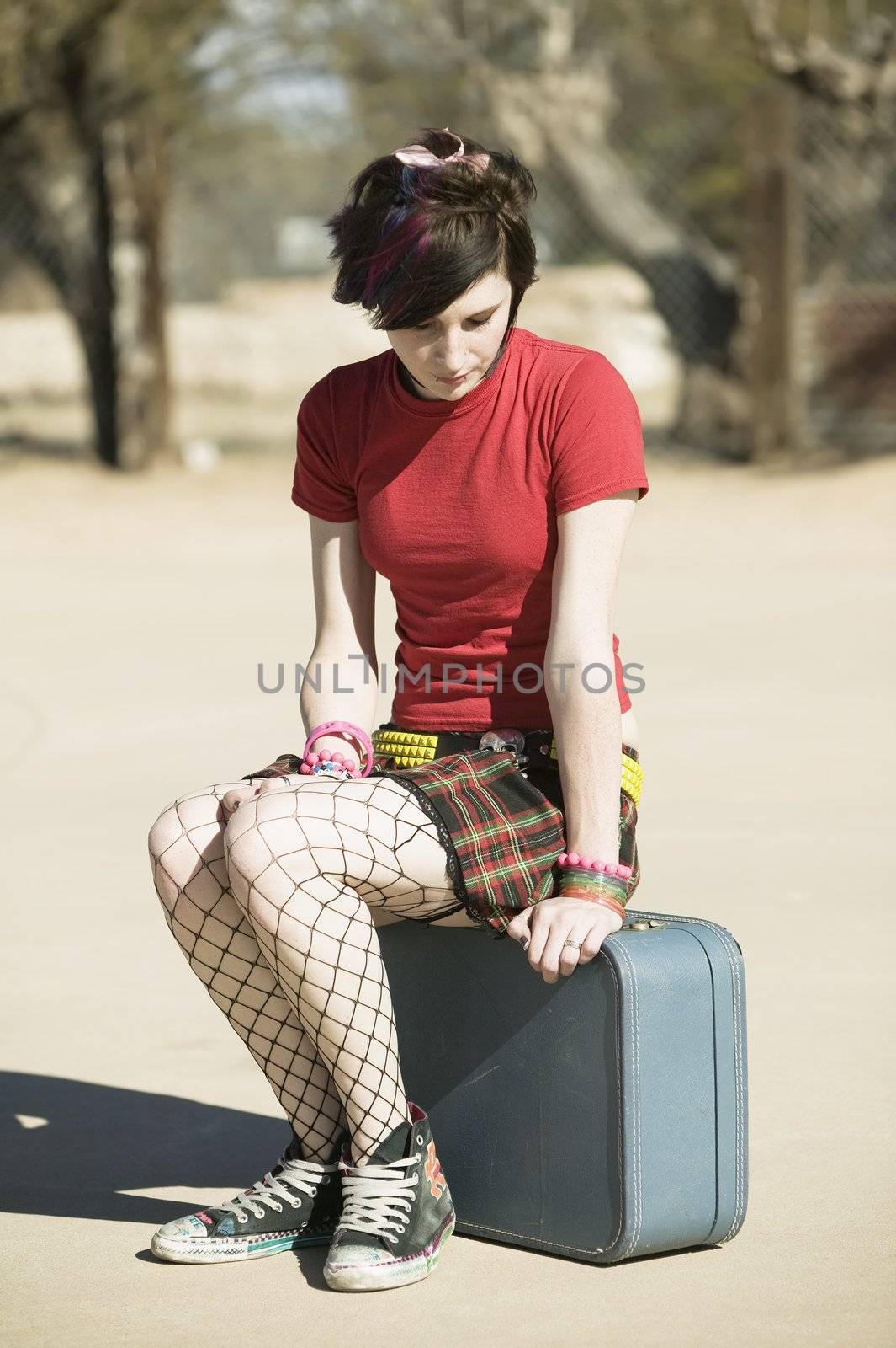 Punk Girl Sitting on a Suitcase on a Cement Playground
